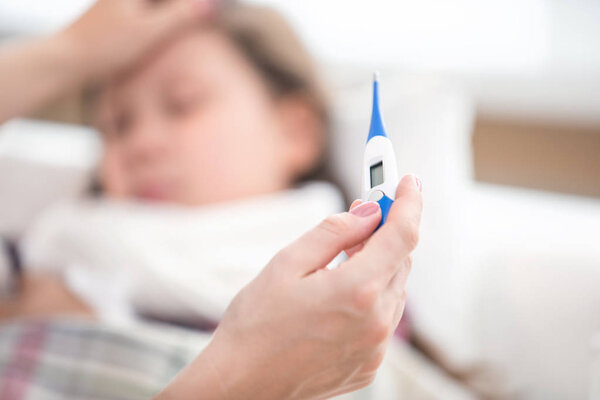 thermometer in the hands of the mother against the backdrop of a sick daughter