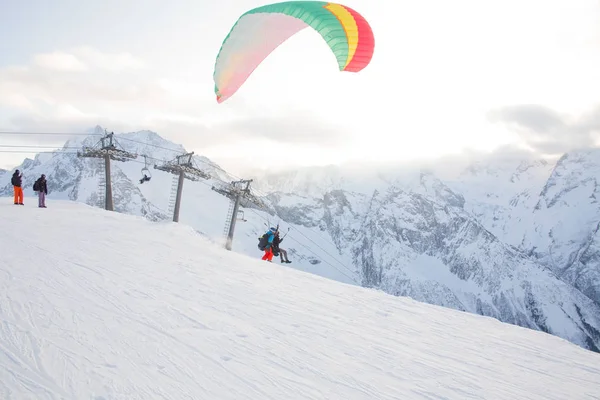 人のインストラクターと雪の山の空を飛んでいる乗客とパラグライダー — ストック写真