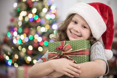 Santa şapka hediye Noel ağacının altında tutarak, küçük kız