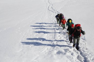 Sırt çantalı bir grup dağcı dağın karlı yamacı boyunca ilerler.
