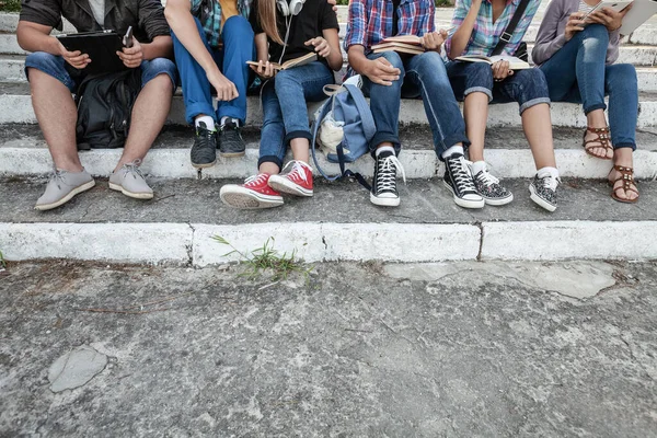 一群拿着书和小玩意的年轻学生坐在公园的台阶上 无法辨认 — 图库照片