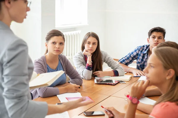 Bir grup öğrenci okuldaki öğretmenleri dinliyor.