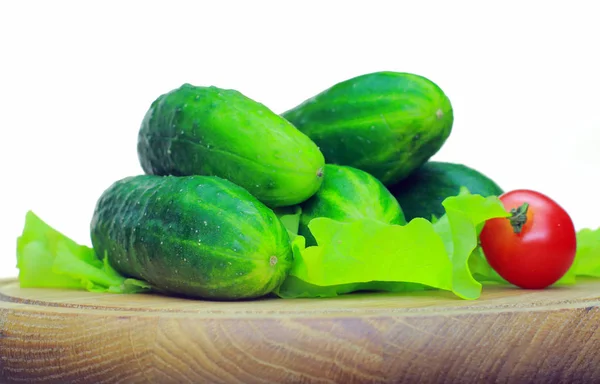 Sur la planche en bois sont les légumes. Tomate, concombre, salade allonge appétissante sur une planche en bois sur fond blanc — Photo