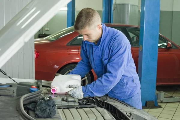 Het vullen van de auto met antivries. Master in de werkplaats opent de tank en giet roze koelvloeistof — Stockfoto