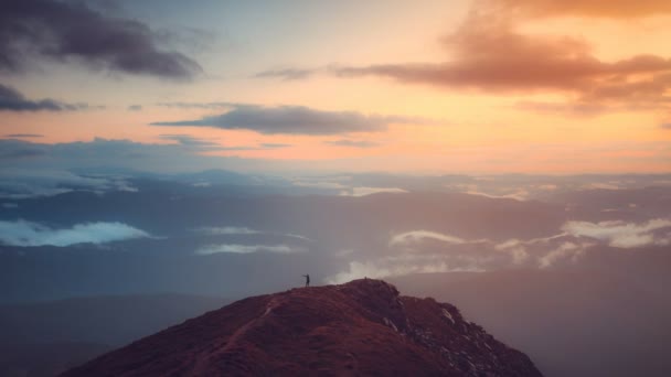 Человек стоит на вершине горы на восходе солнца мягким светом — стоковое видео