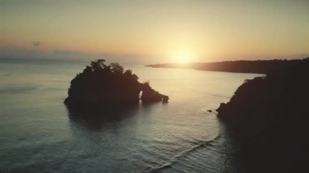 空中无人机飞行从岩山拱门在日落海洋水 美丽的野生海滩湾热带努沙佩尼达岛 印度尼西亚 自然景观 快速运动超限 — 图库视频影像