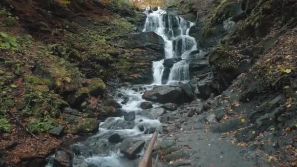 Живописный вспенивающийся водопад около серой дорожки осенью — стоковое видео
