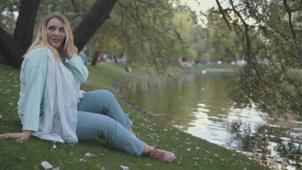 女性プラスサイズのトークスマートフォンが川岸に座る — ストック動画