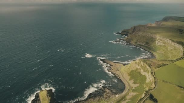 Bahía aérea de Irlanda de arriba hacia abajo: costa de roca verde con amplios prados de hierba, campos y carretera rural — Vídeos de Stock