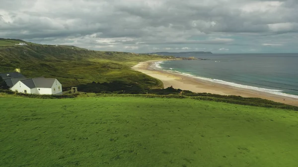 Strandstuga flygfoto: grön äng nära havsvik och ensam White Rocks, Nordirland — Stockfoto