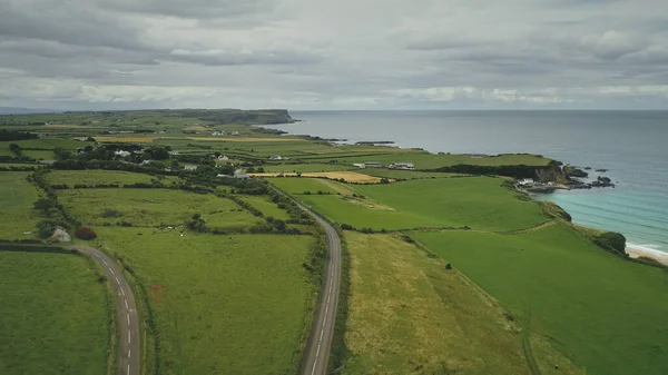 Vista aérea estrada prados verdes panning up. Passeios de carro ao longo do caminho de terras agrícolas no coutryside irlandês — Fotografia de Stock
