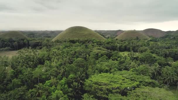 Drone vliegen over het regenwoud naar Chocolate Hills met weelderig groen. Witte huisjes onder bomen bladeren — Stockvideo