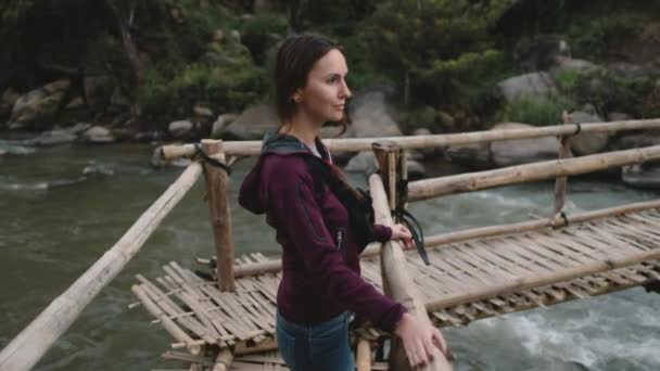 Mulher retrato tailandês ponte da selva tiro. Menina bonita fica, olhando para a paisagem do rio e sorrindo — Vídeo de Stock