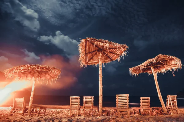 Tropische strandnacht: ligstoel, parasol op zandstrand met sterren aan bewolkte hemel — Stockfoto