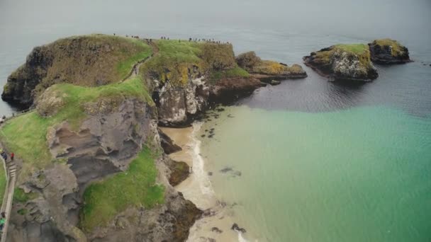 Ireland people ocean bay aerial view: tourists walking on Carrick Islet, Carrick-a-Rede Rope Bridge — Stock Video