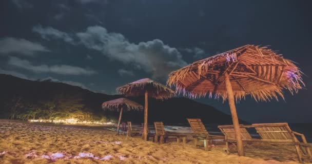 Тімелапс нічні пляжні парасольки на березі океану. Пальмові дерева кафе на узбережжі біля морської бухти — стокове відео