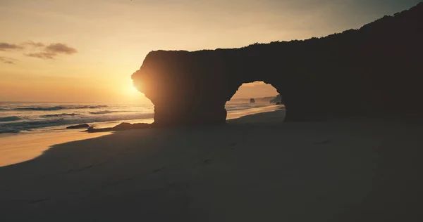모래사장의 바위 벽에 구멍이 뚫려 있는 태양 빛 실루엣. 공중의 해변 관광 명소 — 스톡 사진