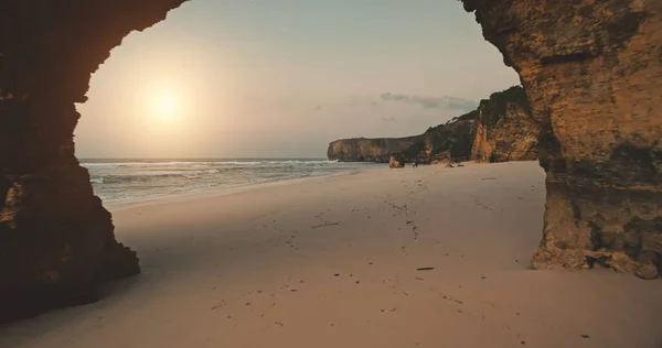 Olbrzymia dziura w ścianie klifu lot dronem do piaszczystej plaży nad zatoką oceanu z chodzącymi turystami widok z lotu ptaka — Zdjęcie stockowe