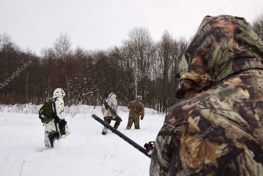 Group of hunters in winter forest with carbines and shotgun at dawn