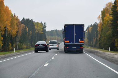 Karelia, Rusya - 30 Eylül 2020: Kamyon ve diğer arabalar sonbahar ormanı boyunca otoyol boyunca ilerliyorlar. Kola yolu. Manevrayı aşıyorum.