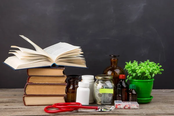 Medical education concept - money glass, books, pharmacy bottles, blackboard behind