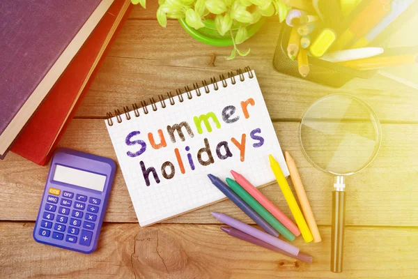 summer holidays inscription with colored crayons and notepad on the wooden table