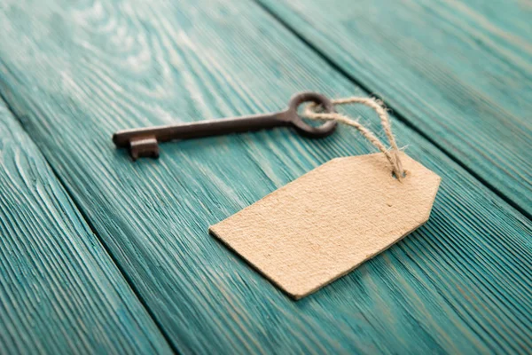 Oude roestige sleutel met een papieren etiket op de houten plank — Stockfoto