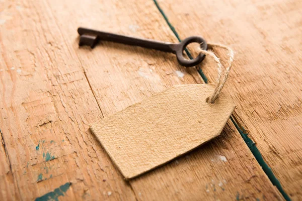 Vecchia chiave arrugginita con etichetta di carta sul pannello di legno — Foto Stock