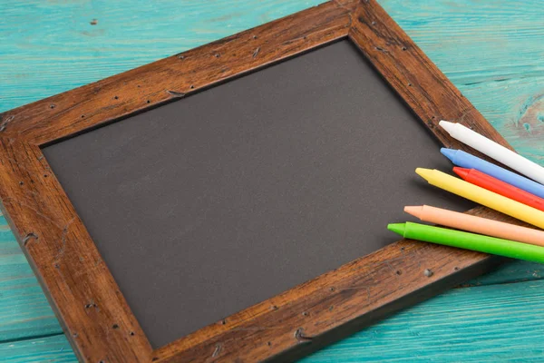 Leeg schoolbord met copyspace en kleurrijke kleurpotloden op houten tafel — Stockfoto