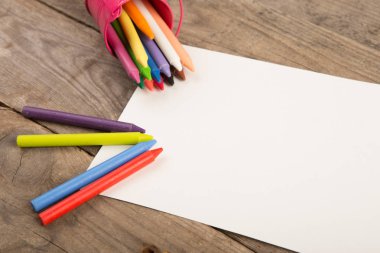 Boya kalemleri ve ahşap masada boş bir sayfa.