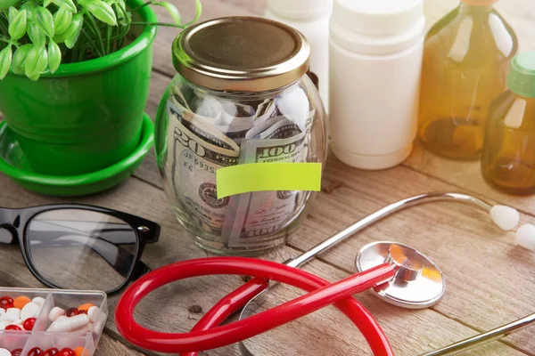 Ahorro de dinero para el seguro de salud - vidrio de dinero, estetoscopio, pastillas y botellas —  Fotos de Stock