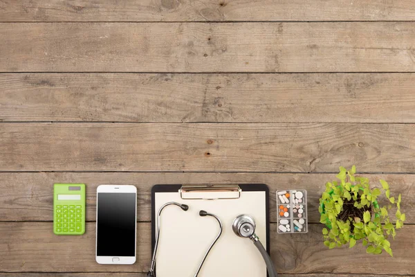 Arbeitsplatz eines Arztes. Stethoskop, Klemmbrett, Pillen, Smartphone und andere Dinge auf dem Holztisch — Stockfoto