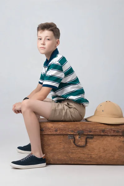 El chico está sentado en una maleta mientras espera — Foto de Stock