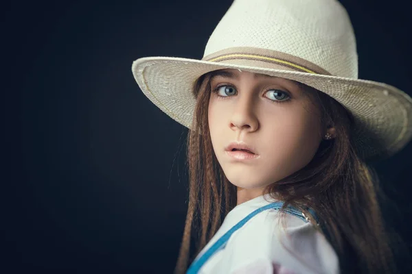 Little girl in denim overalls and straw hat in studio — Stock Photo, Image