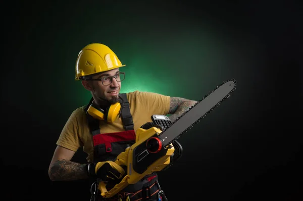 Een jonge man poseren op een zwarte achtergrond in een uniforme werk en een bouw hulpprogramma macht zag — Stockfoto