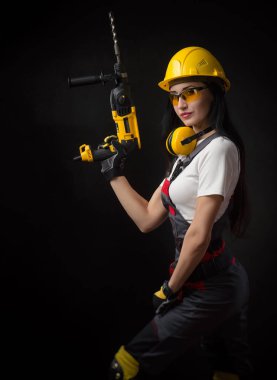 özel giysiler içinde esmer kız ve bir çalışma aracı ile siyah bir arka plan üzerinde poz bir kask bir işçi (perforatör, matkap, perküsyon çekiç )