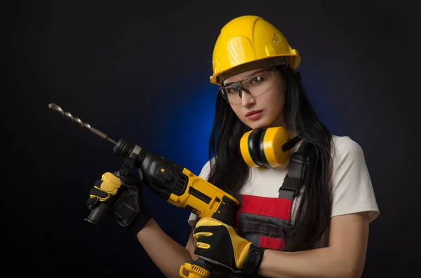 身着特殊服装的黑发女孩和一名戴着头盔的工人在黑色背景上摆出工作工具 穿孔器 打击锤 — 图库照片
