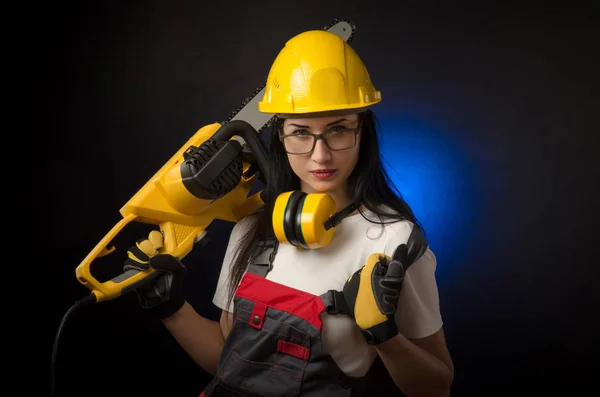 Brunette meisje in speciale kleding en een werknemer in een helm poseren op een zwarte achtergrond met een werkende tool — Stockfoto