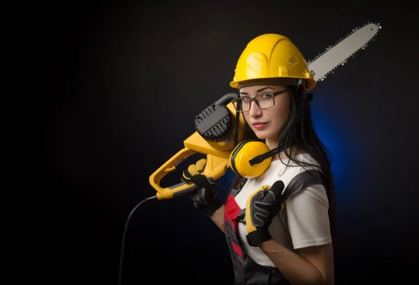 Brunette meisje in speciale kleding en een werknemer in een helm poseren op een zwarte achtergrond met een werkende tool — Stockfoto