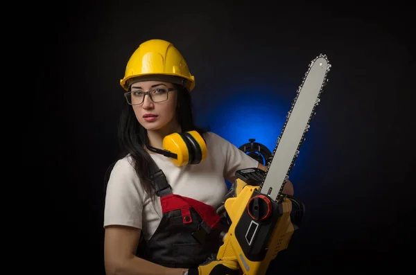 Brunette meisje in speciale kleding en een werknemer in een helm poseren op een zwarte achtergrond met een werkende tool — Stockfoto