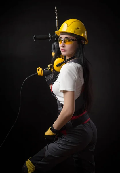 Brunette meisje in speciale kleding en een werknemer in een helm poseren op een zwarte achtergrond met een werkende tool — Stockfoto