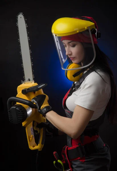 Brunette meisje in speciale kleding en een werknemer in een helm poseren op een zwarte achtergrond met een werkende tool — Stockfoto