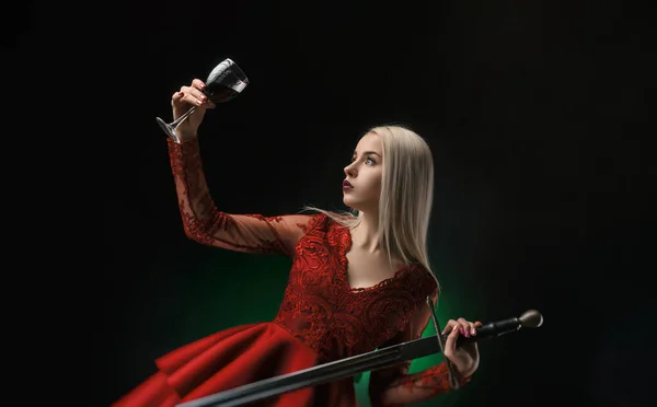 Bir kılıç ve bir kadeh şarap kırmızı elbiseli güzel kız — Stok fotoğraf