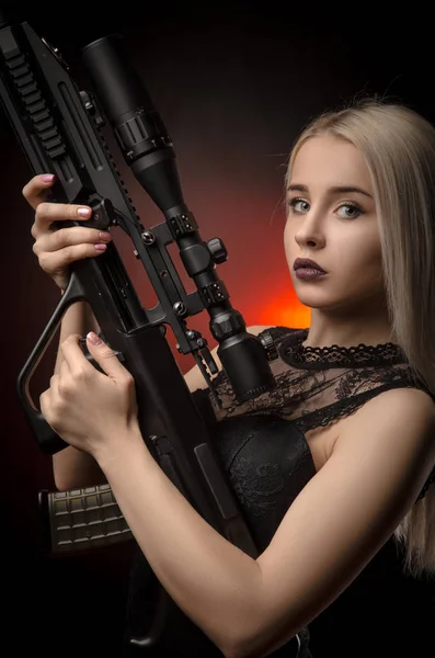 Jovem loira menina em vestido preto posando no fundo preto com arma — Fotografia de Stock