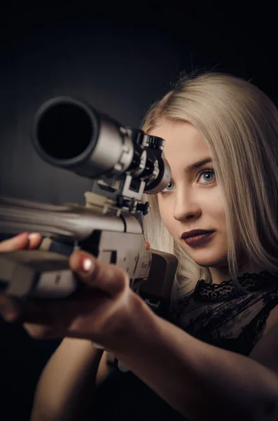 Молодая блондинка в черном платье позирует на черном фоне с оружием — стоковое фото