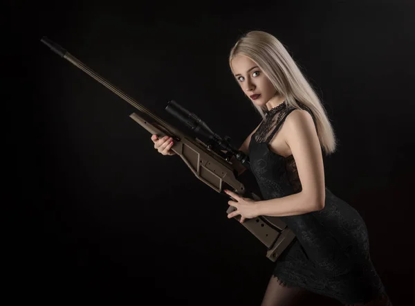 Ung blond tjej i svart klänning poserar på svart bakgrund med vapen — Stockfoto