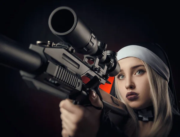 Flicka på en svart bakgrund i en nunna klä poserar med en pistol, siktar, skytte — Stockfoto