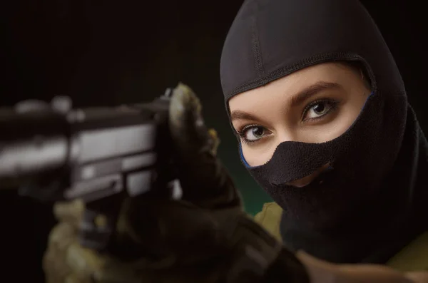 A menina em roupas militares especiais posando com uma arma em suas mãos em um fundo escuro na névoa — Fotografia de Stock