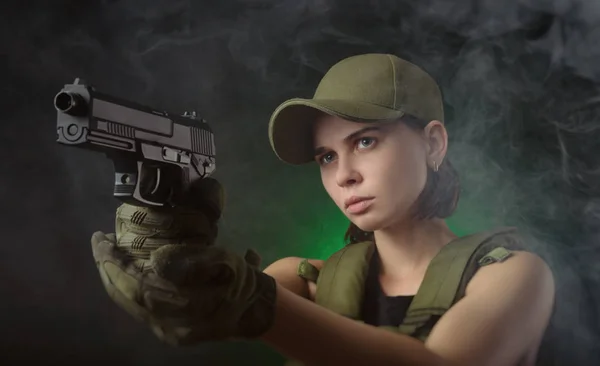 Flickan i militära speciella kläder poserar med en pistol i händerna på en mörk bakgrund i diset — Stockfoto