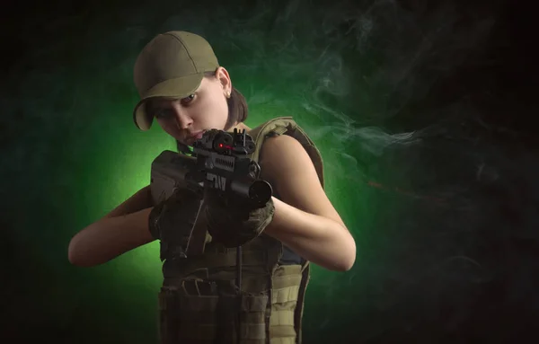 La chica con ropa militar especial posando con un arma en sus manos sobre un fondo oscuro en la niebla —  Fotos de Stock